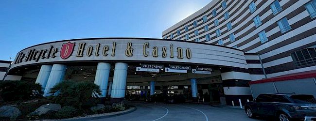 This image features the entrance of a hotel and casino, with the building's name prominently displayed above the entrance, under a clear sky.