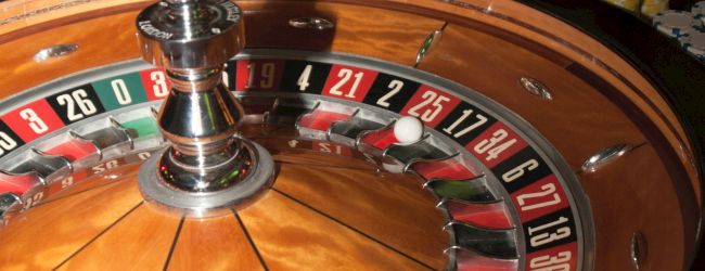 A roulette table at a casino is shown, with people placing chips on the table and the roulette wheel in focus, ready for the next spin.