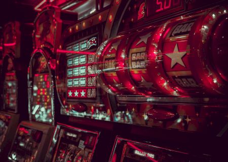 The image shows a row of slot machines in a dimly lit room, with bright lights and displays featuring 