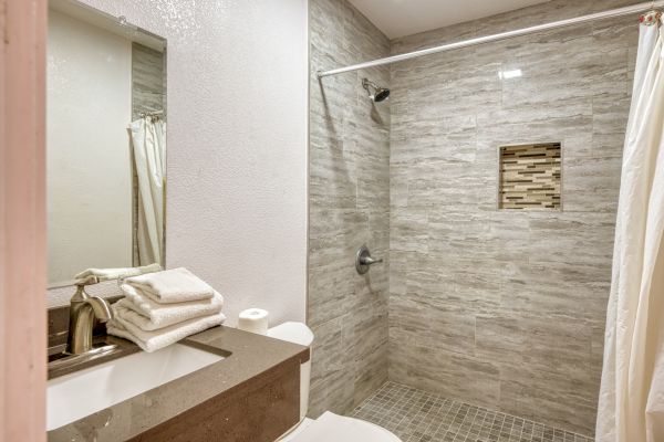 A modern bathroom with a tiled walk-in shower, vanity with sink, stacked towels, and a shower curtain rod without a curtain.