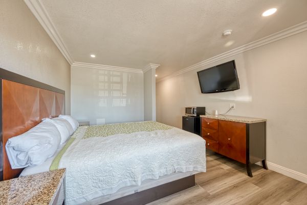 A hotel room with a bed, wall-mounted TV, dresser, microwave, and mini-fridge, featuring modern decor and wooden flooring.