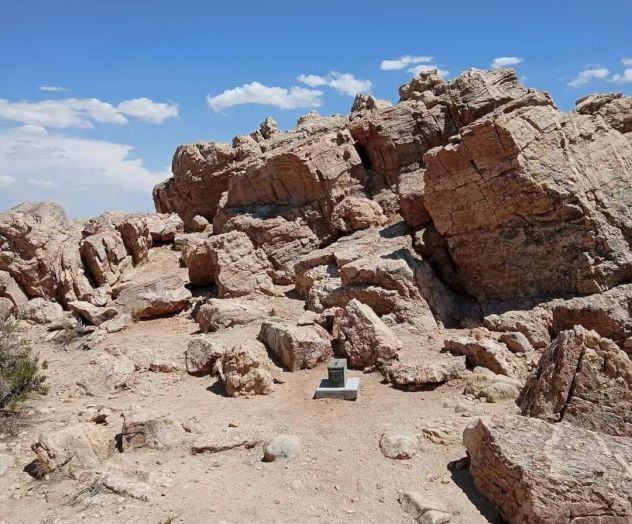 A rocky desert terrain with large boulders scattered around and a small monument or box-like structure located in the middle.