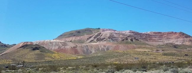 The image shows a semi-arid landscape with a road in the foreground, scrub vegetation, and a mountain range with visible layers in the background.