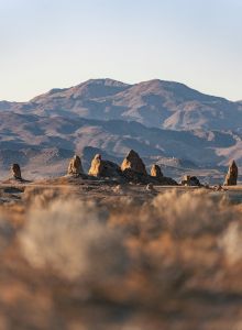 A desert landscape with rocky formations in the foreground and mountains in the background under a clear sky.