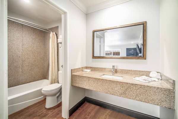 A modern bathroom features a toilet, a bathtub with a shower curtain, a countertop sink, mirror, and clean towels on a wooden floor.