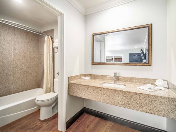 A modern bathroom features a toilet, a bathtub with a shower curtain, a countertop sink, mirror, and clean towels on a wooden floor.