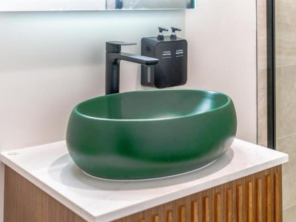 A green oval sink sits on a white countertop with a black faucet and soap dispenser attached to the wall.