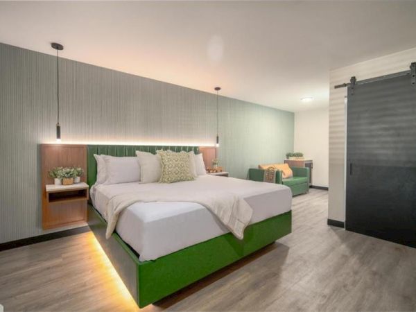 A modern bedroom with a double bed, green accents, pendant lights, and a sliding door, featuring a cozy seating area.
