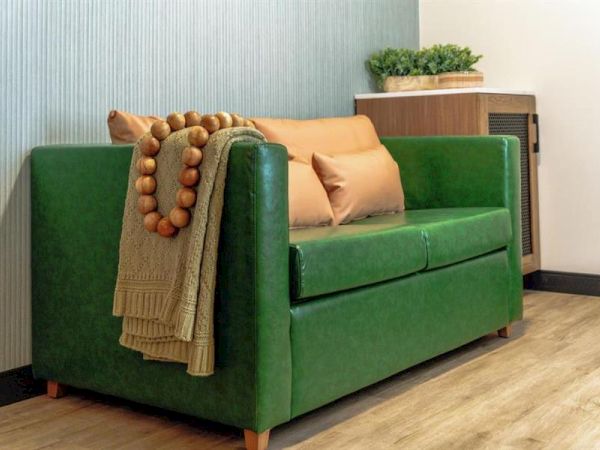 A green couch with pillows and a blanket, adorned with a beaded garland, sits on a wooden floor near a small table with plants.