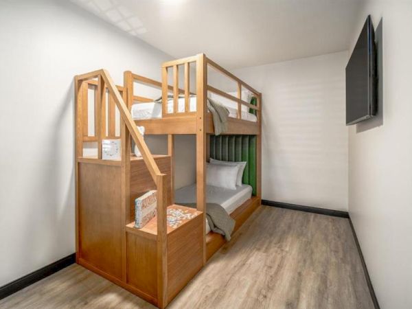 The image shows a clean, minimal room with a wooden bunk bed and a wall-mounted TV on the right side.