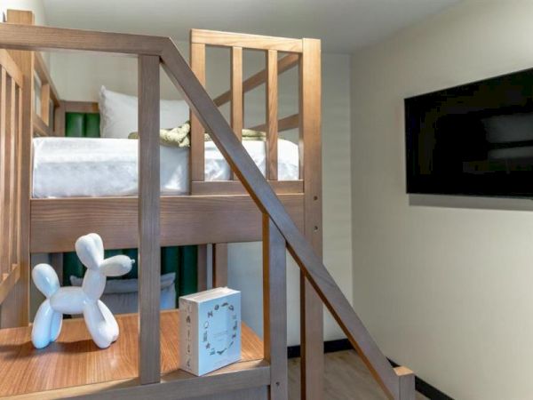 A room with bunk beds, a wooden staircase, a plush toy, a small cube, and a wall-mounted flat-screen TV.