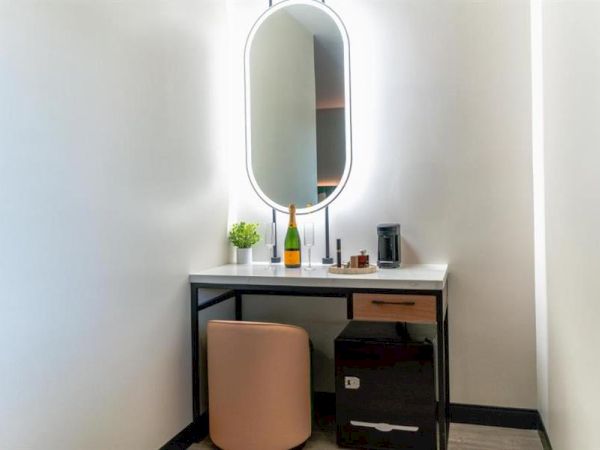 A vanity setup with a lighted mirror, chair, and various items like a plant and bottles on the table, in a corner space.