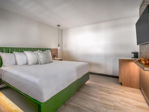 A modern bedroom with a green bed, white bedding, wall-mounted TV, wooden furniture, and soft lighting.