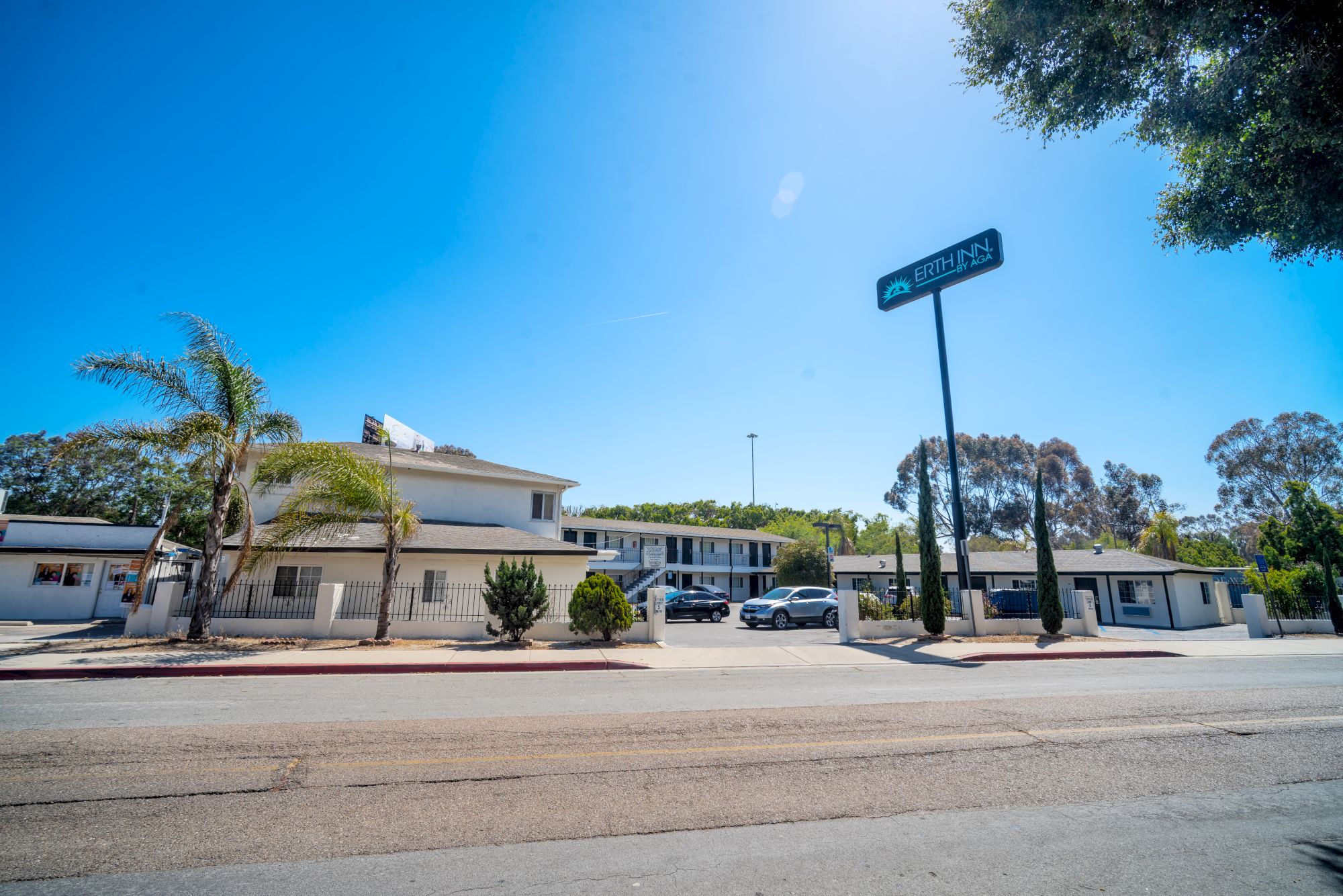 The image shows a roadside motel with a sign reading "Oasis Inn & Suites" under a clear blue sky with some parked cars.