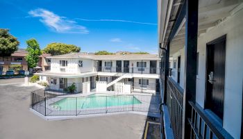 Image of a two-story motel with a central swimming pool, surrounded by a black fence, and clear blue skies above the building.