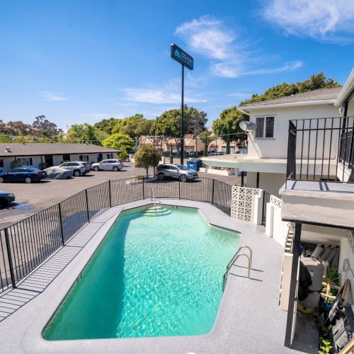 The image shows a motel courtyard with a pool surrounded by railings, cars parked, and a building with two stories.