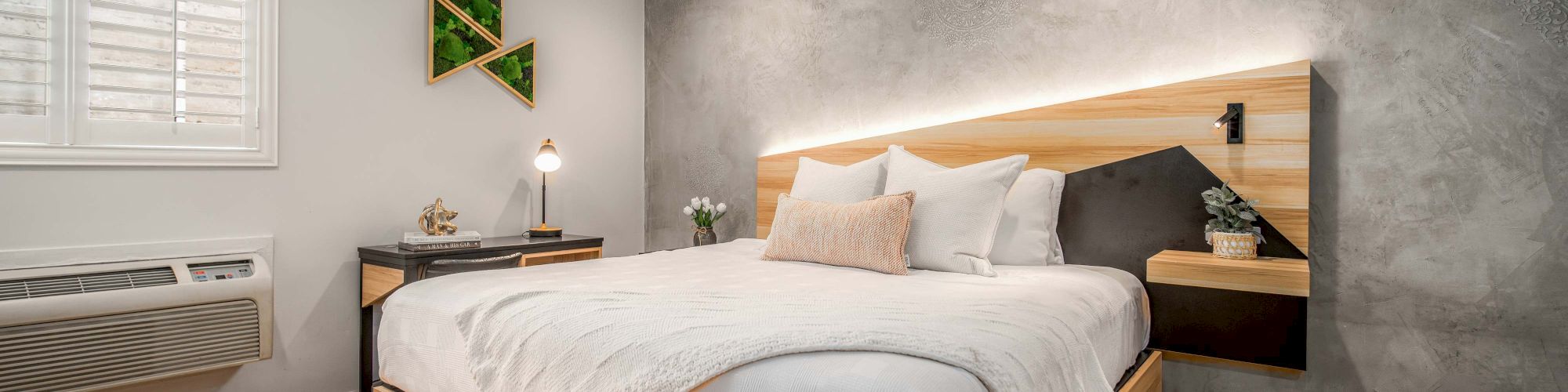 A modern bedroom with a wooden bed, white bedding, gray accent wall, side tables, warm wood floor, and soft lighting.