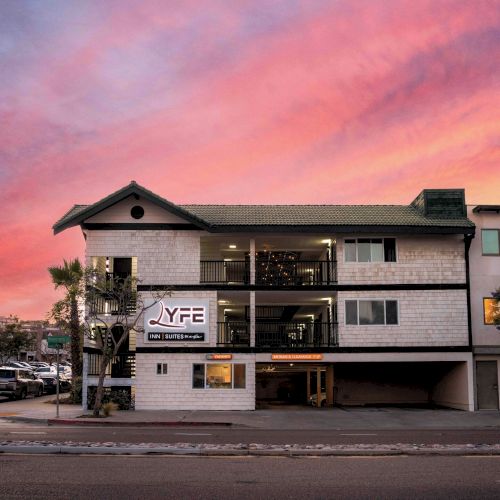 A three-story white brick building with a parking area underneath, a sign &ldquo;YF&rdquo; on the left, and a dramatic pink sunset sky.