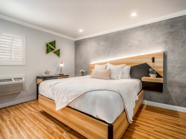 A modern bedroom with a wooden bed, gray accent wall, white bedding, two nightstands, and warm wooden floors, bright and cozy atmosphere.