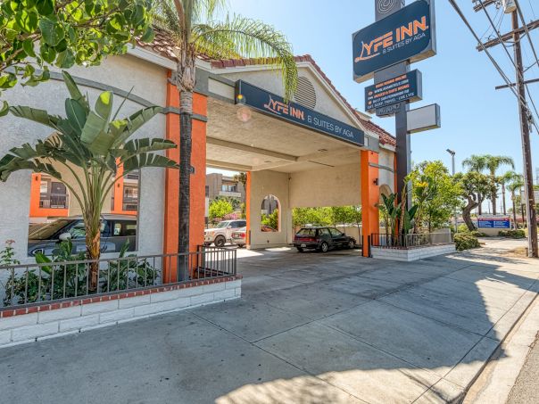 A My Inn hotel exterior with a covered drive, palm trees, signage, and a sunny street view; inviting entry under a bright orange-trimmed canopy.