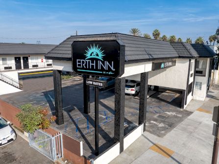 A small motel called Earth Inn with black framing, a sign, and a blue sky; exterior with parking and white buildings, low-rise.