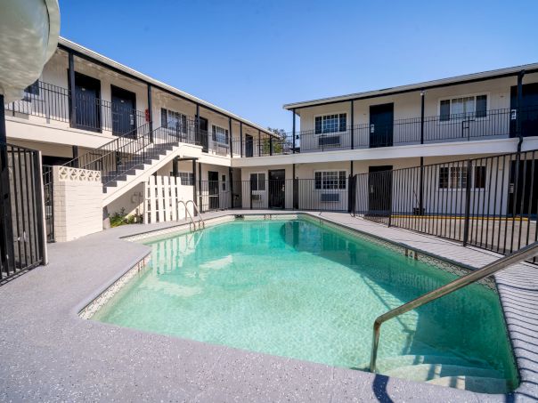 A small motel-style courtyard with a rectangular swimming pool, surrounded by two-story beige buildings and metal railings.
