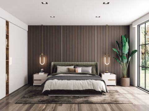 A modern bedroom features a bed with green and white bedding, hanging lights, wooden accents, and large windows. A potted plant adds greenery.