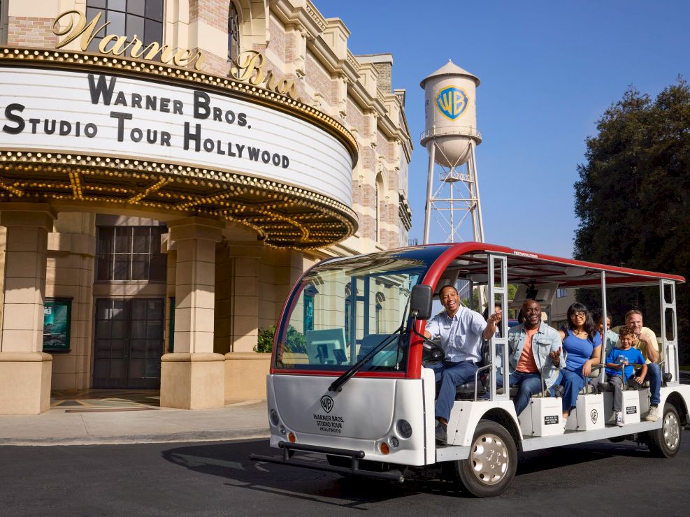 A Warner Bros. Studio Tour Hollywood bus carries a group of visitors parked outside the Warner Bros. building.
