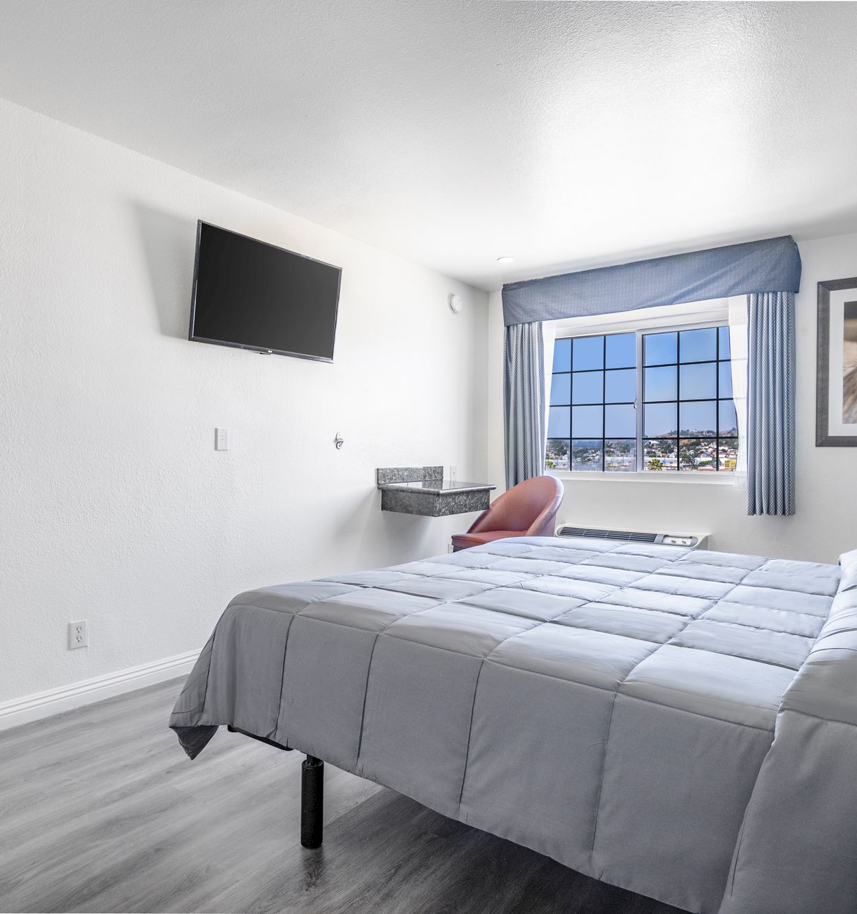 A modern bedroom with a large bed, wall-mounted TV, blue window curtains, framed horse photo, and city view through the window.