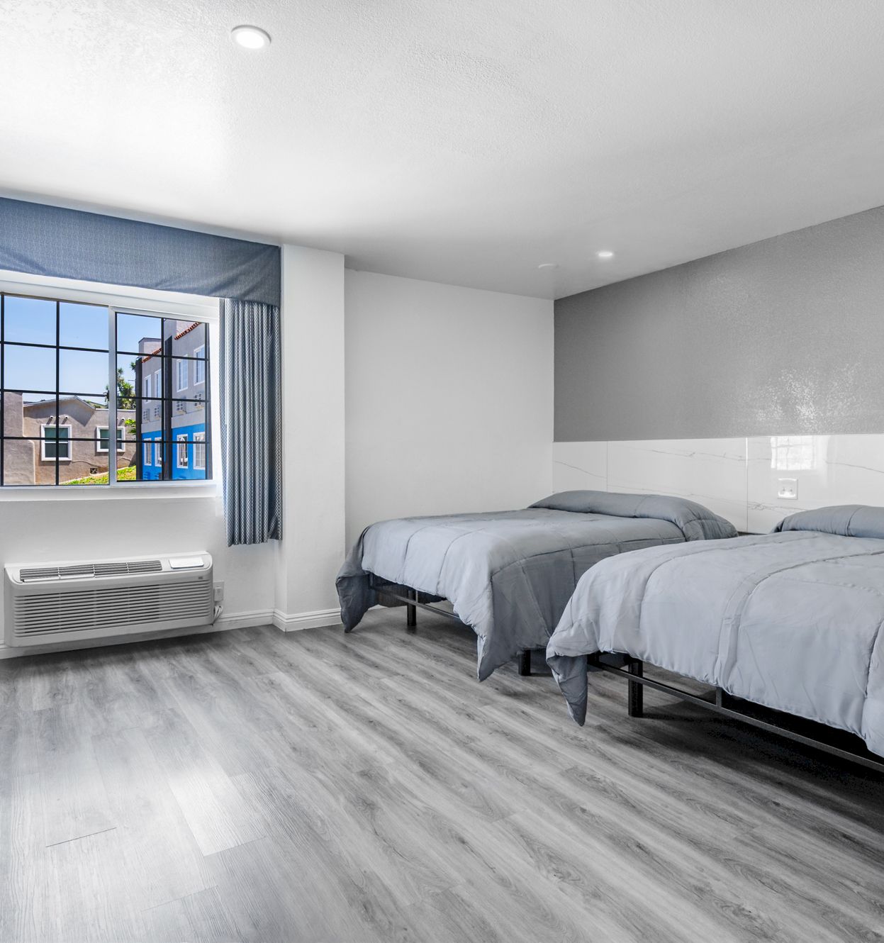 A modern bedroom with two twin beds, gray curtains, a window, and a brown chair near the radiator.