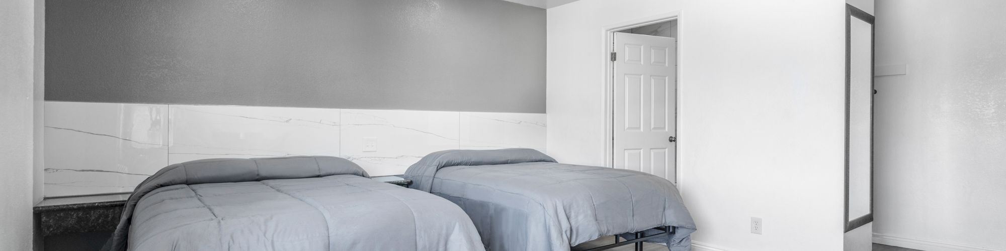 A modern bedroom with two twin beds, gray-and-white wall paneling, recessed lights, and a white interior door.