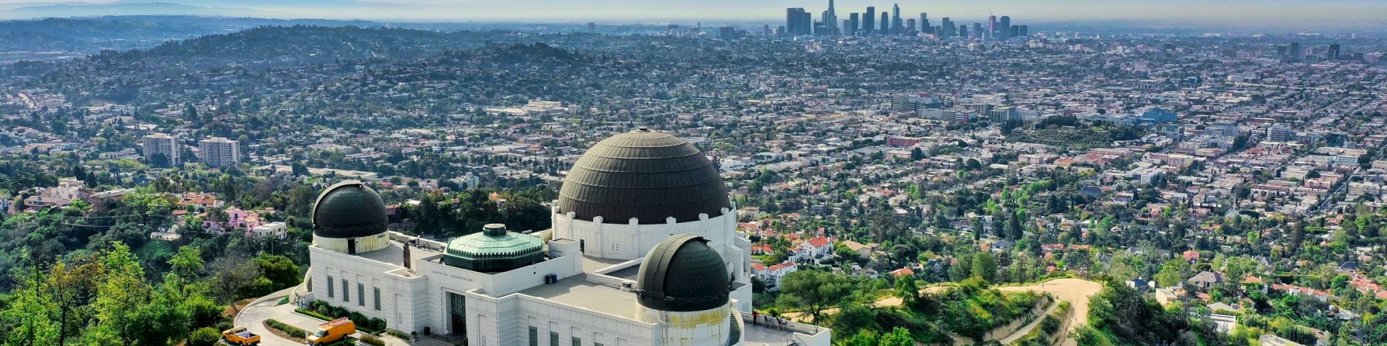 Aerial view of a white observatory with domes overlooking a sprawling city skyline under blue sky.