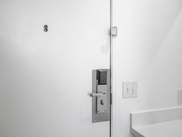 An interior wall shows a metal door handle and lock with a wall outlet and switch nearby.