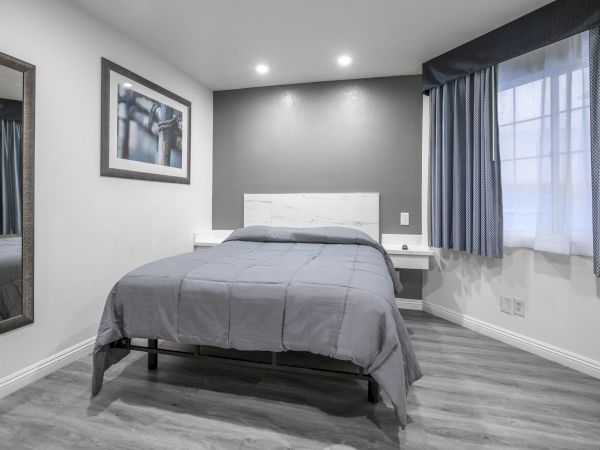 A modern bedroom with a gray bed, framed wall art, striped curtains, and recessed ceiling lights.