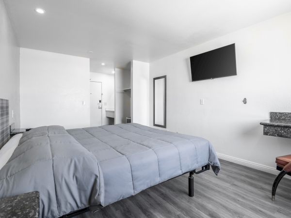 Bright modern bedroom with a large bed, wall-mounted TV, mirror, and small stone countertop.