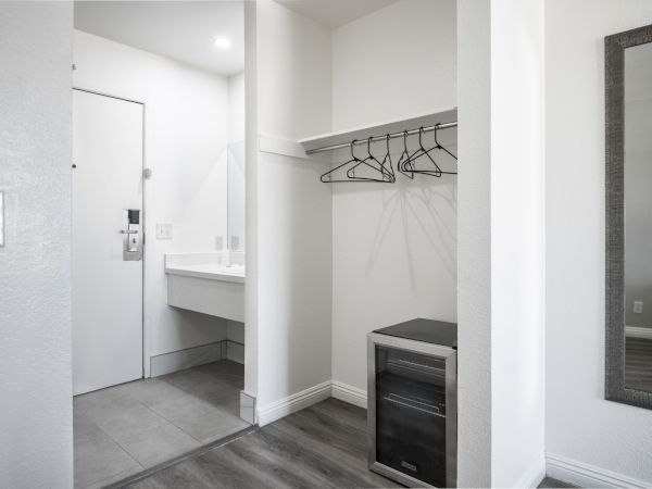 A bright closet with hanging rods, empty hangers, tiled floor, and a bathroom doorway with a sink in view.