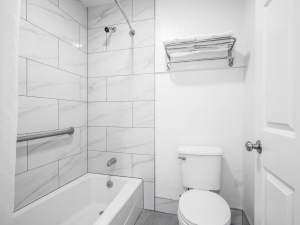 Black-and-white bathroom with marble tiles, shower/tub combo, chrome showerhead, towel bar, and a white toilet.