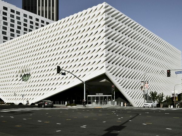 A street view of The Broad museum, showing its striking white, wave-like perforated fa&ccedil;ade above traffic lights and cars.