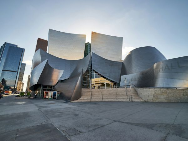 A dramatic stainless-steel concert hall fa&ccedil;ade with stepped stairs and nearby downtown buildings, likely the LA Phil&rsquo;s Walt Disney Concert Hall.
