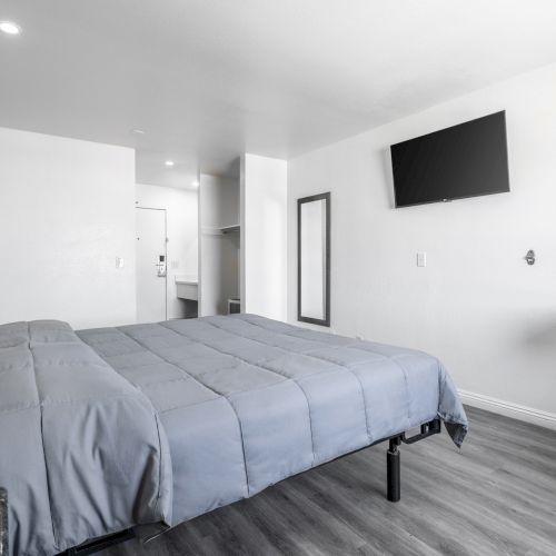A modern bedroom with a made bed, wall-mounted flat-screen TV, mirror, and a small granite ledge by a chair.