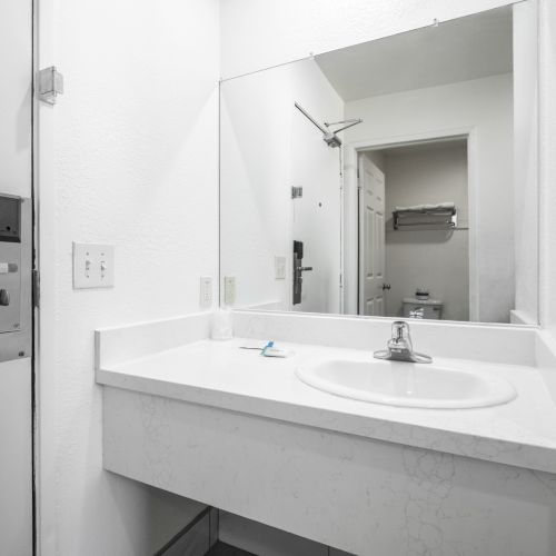 A modern bathroom with a wall mirror, sink vanity, faucet, and a visible toilet area through an open door.