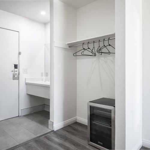 A clean walk-in closet with a hanging bar, coat hangers, tiled floor, and nearby shelves in a modern room.