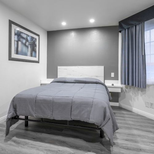 A modern bedroom with a gray bed, framed wall art, blue-striped curtains, and a large wall mirror.