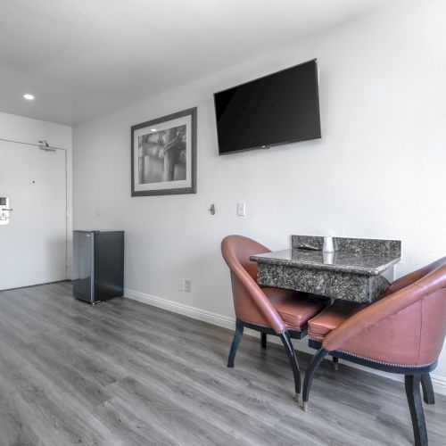 A modern office/lounge with a wall-mounted TV, framed photo, granite desk table, leather chairs, and a door and thermostat.