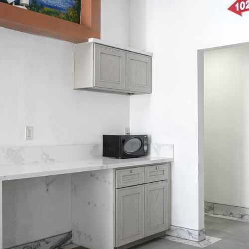 A clean utility room with white wall cabinets and a microwave on a marble countertop, plus outlets and a &ldquo;102-108&rdquo; sign.