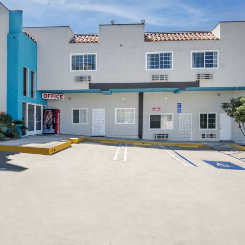 A bright exterior office building with blue trim, windows, a &ldquo;OFFICE&rdquo; sign, and marked parking spaces in front.