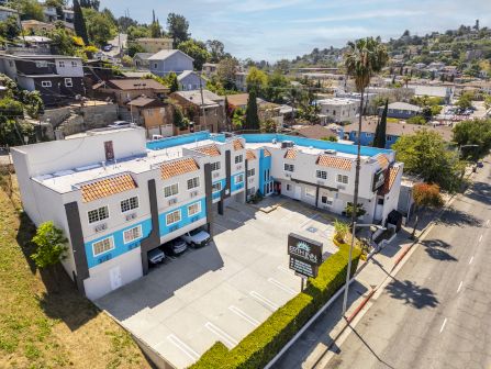 Aerial view of the Earth Inn hotel complex with blue-and-white buildings, orange tile roofs, parking lot, and courtyard pool.